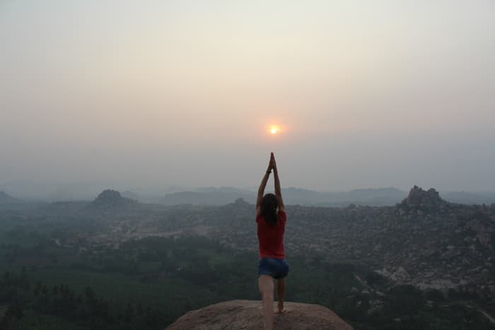 Standing with palms pressed overhead as the sun rises over the boulder fields